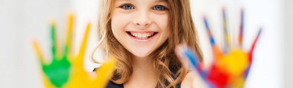 Smiling young girl holding up hands covered in bright paint