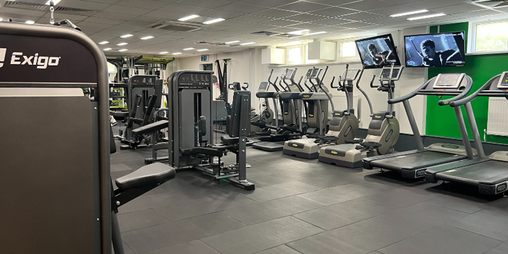 A row of treadmills, cross trainers, and cycle machines against a wall in a gym, and other cardiovascular machines in the centre.