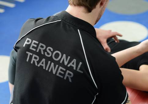 Man wearing t-shirt saying 'Personal trainer' helping women who is doing crunches on a exercise ball