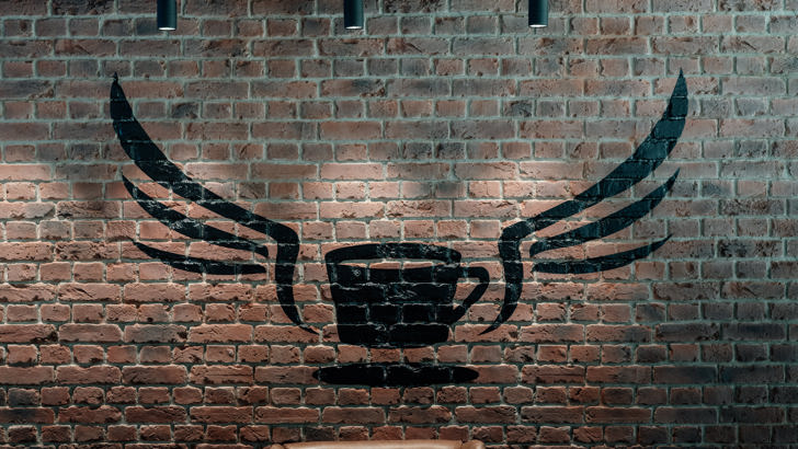 Brick wall with painted with large decorative coffee cup with wings