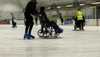 Young woman on ice skates in an ice rink, pushing a person in a wheelchair along on the ice preview