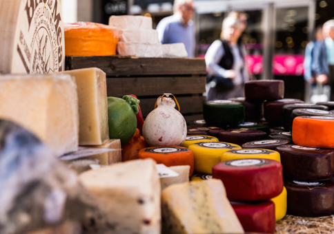 People looking at various cheeses laid out on a market stall