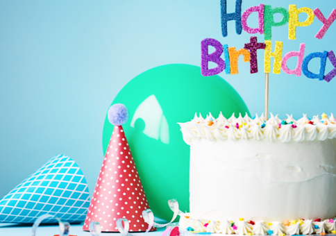 Cake featuring a 'Happy birthday' topper, surrounded by balloons, party hats and streamer