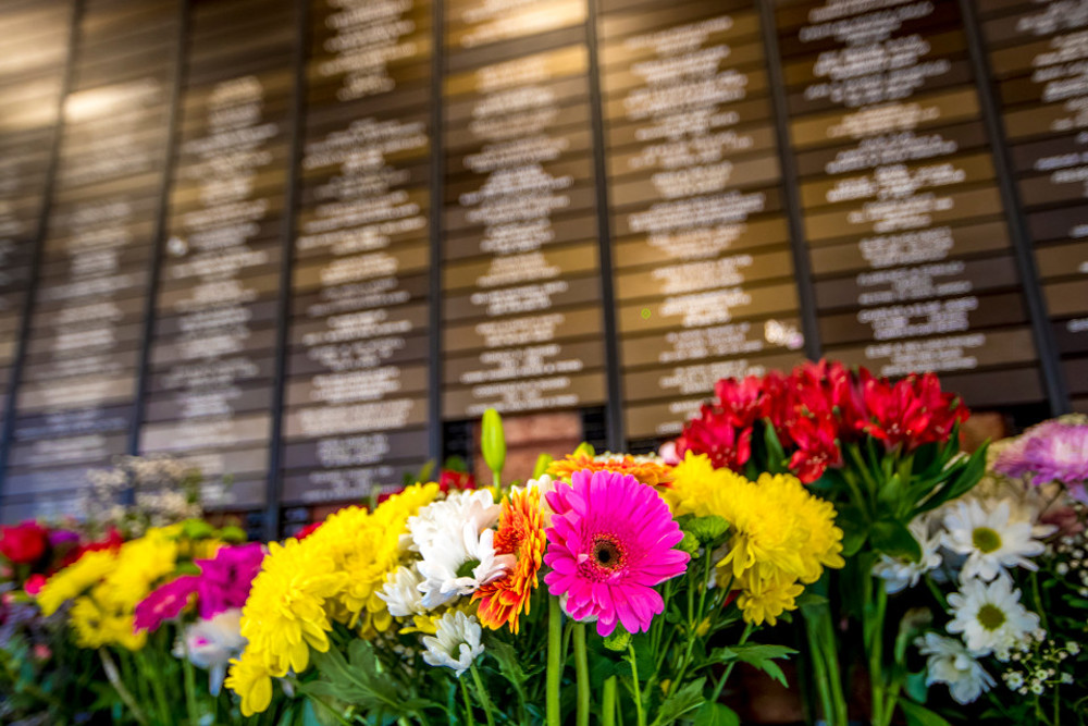 Colourful flowers in front of wall full of small plaques bearing the names of deceased loved ones