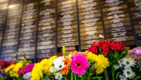 Colourful flowers in front of wall full of small plaques bearing the names of deceased loved ones preview