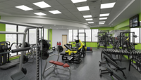 A digitally rendered image of how the CSAC gym should look once refurbished, showing rows of weights machines, benches and weight racks next to a range of free weights including dumbbells and kettle bells against a mirrored wall. The area is brightly lit with large square downlights. preview