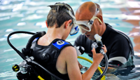 Male instructor checking boy's scuba equipment in swimming pool preview