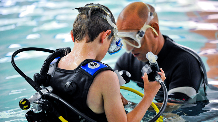 Male instructor checking boy's scuba equipment in swimming pool