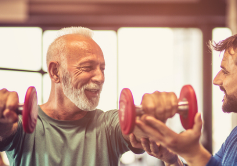 Personal trainer helping older man who is holding small dumbbells