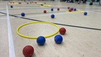 red and blue Boccia balls on the floor of a sports hall, next to a yellow hoop preview