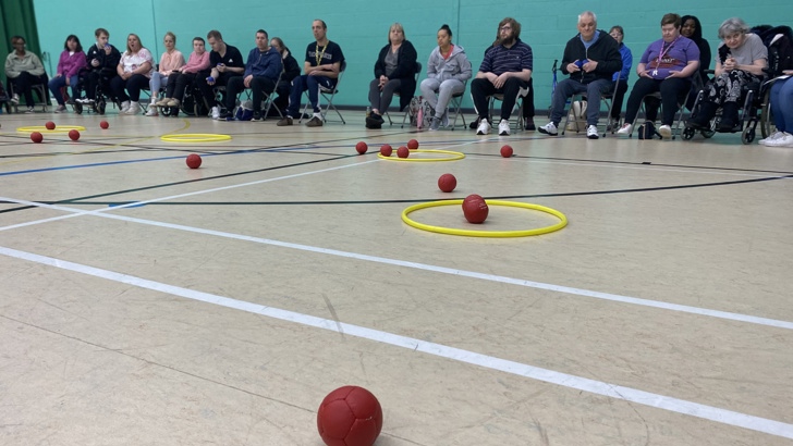 red Boccia balls on the floor of a sports hall next to a yellow hoop