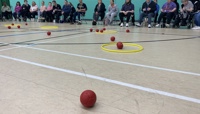 red Boccia balls on the floor of a sports hall next to a yellow hoop preview