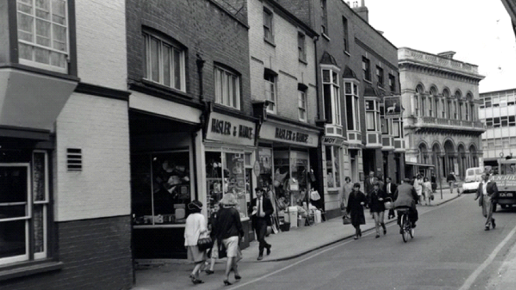 People walking past row of shops (black and white photo from 1958)
