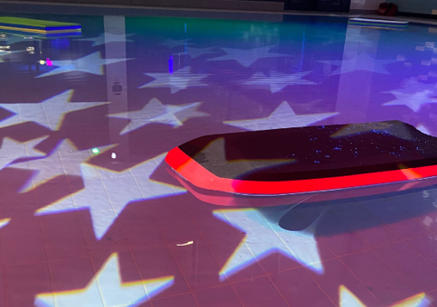 Body board floating in pool, with disco lights in the shape of stars projected on surface of water