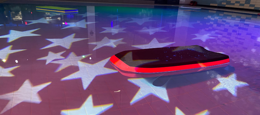 Body board floating in pool, with disco lights in the shape of stars projected on surface of water