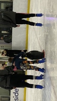 Young boy learning to ice skate, holding onto a penguin aid, with coaches either side. preview