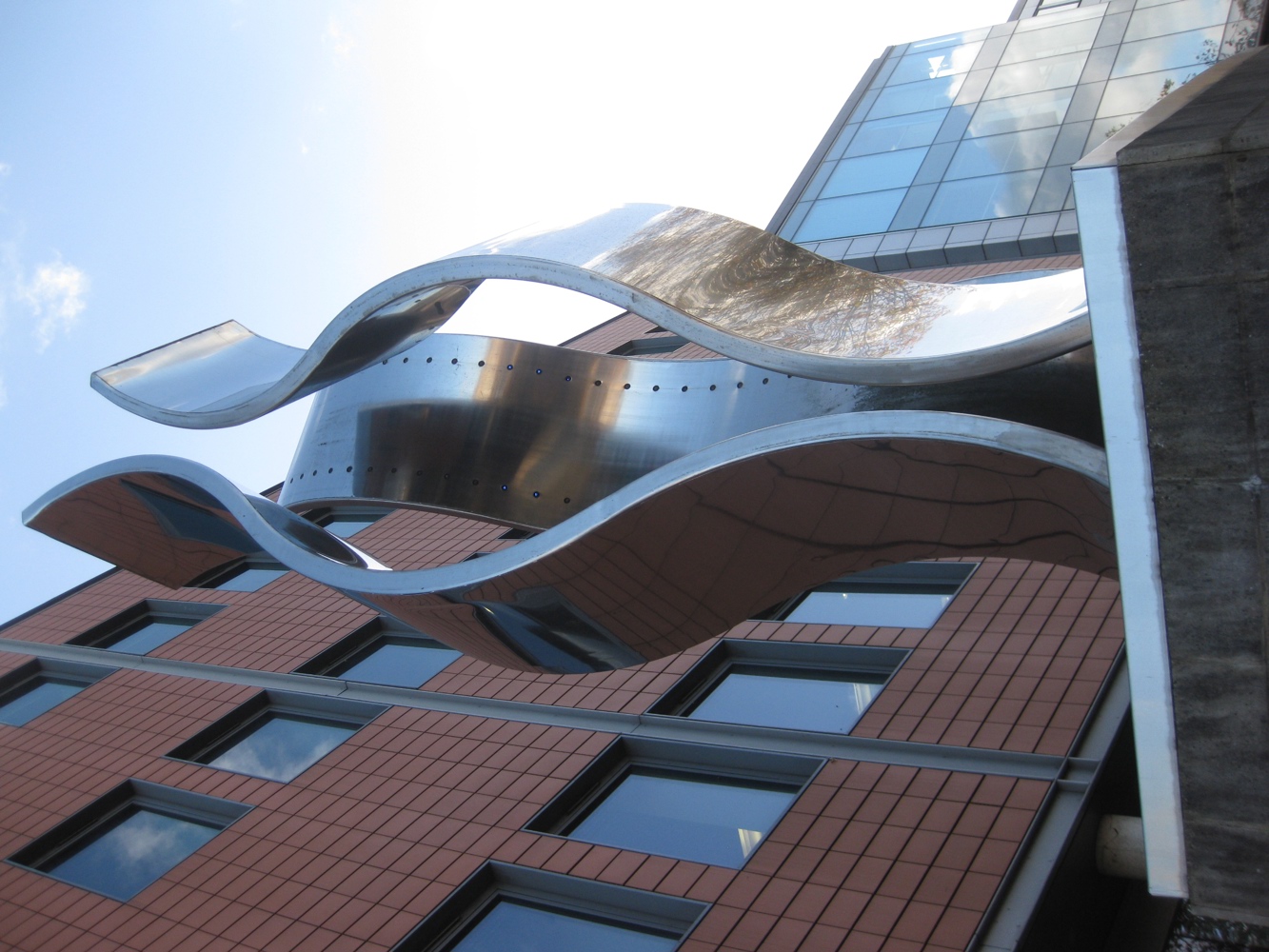 Statue featuring three large, vertical, stainless-steel ribbons, one with blue LED lights lining the inner surface