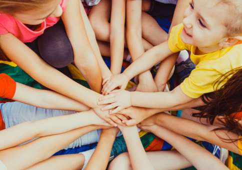 Group of children in a circle, putting their hands together in the middle