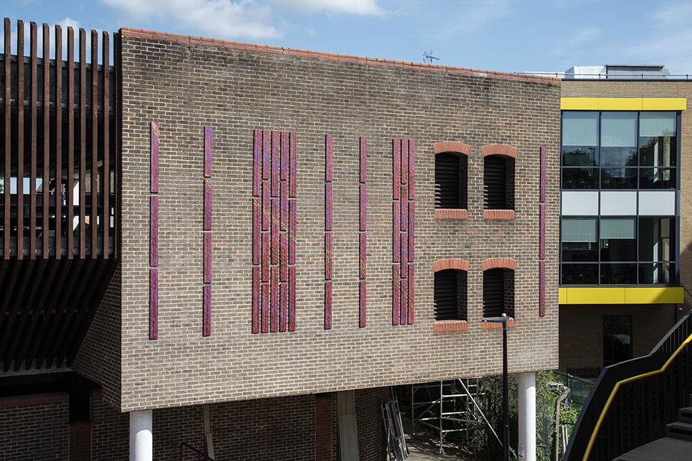 Tall, vertical, copper panels on outside brick wall of car park