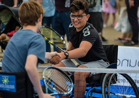Two older boys in wheelchairs shaking hands over the net on a tennis court