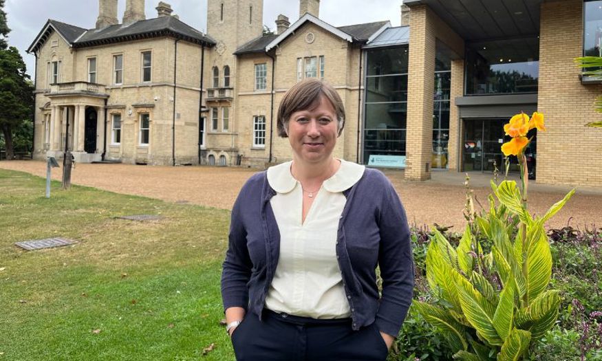 A woman with short brown hair smiles at the camera while stood outside of Chelmsford Museum. 